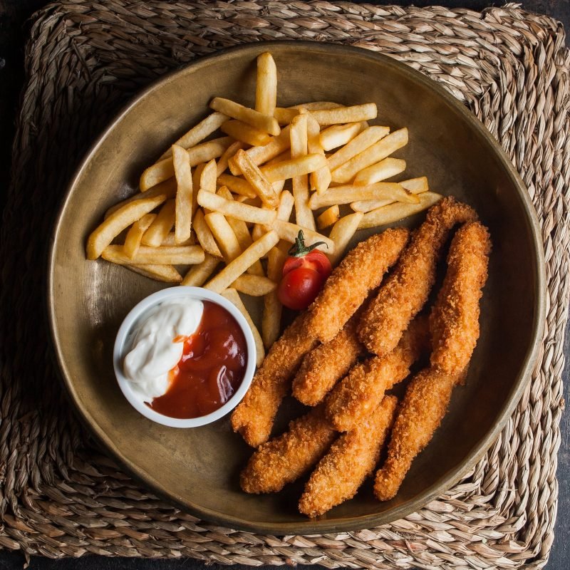 Top view chicken nuggets with french fries and tomato and sous in clay dishes on stone background